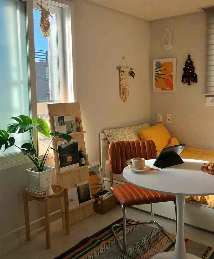 暖かいベージュとブラウンのトーンのワンルーム、木製家具と黄色の寝具、ラグと椅子が配置された居心地の良い朝の空間