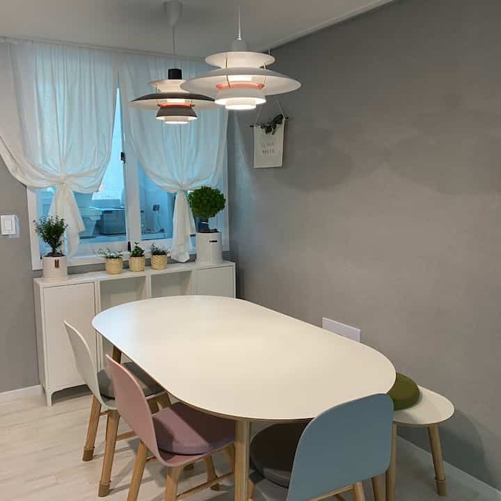 グレーの壁とホワイト家具が調和したダイニングルーム、楕円形のダイニングテーブルと多色の椅子が配置されたナチュラルモダンな空間