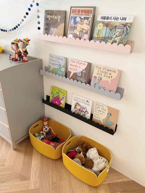 Kids' room with yellow and natural color tones featuring toy storage baskets and wall-mounted bookshelf with children's books, neatly organized