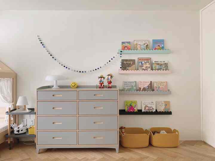 Monotone toned kids' room featuring a gray dresser, pastel-colored shelves, and mustard storage baskets in a baby-friendly space