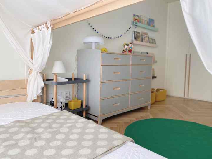Natural-toned kids' room with wood flooring, featuring a house-shaped bed, light gray dresser, and green round rug creating a cozy atmosphere