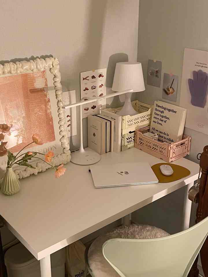 Beige and ivory toned single household desk space featuring a table lamp and posters creating a cozy study and reading area