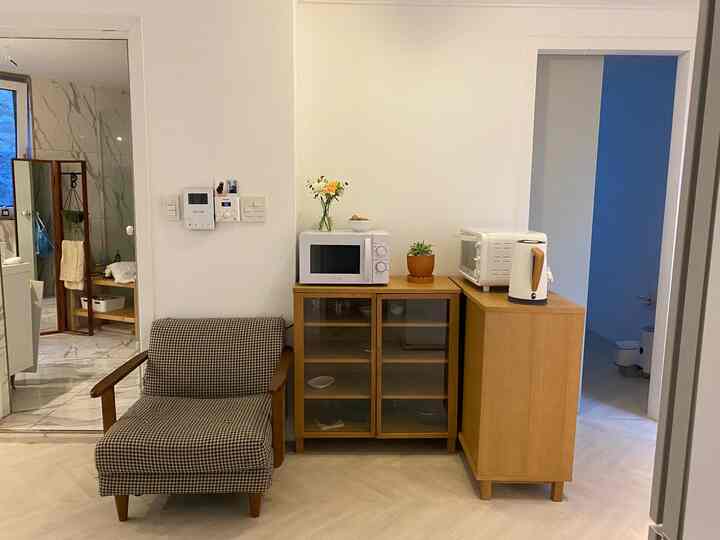 White and brown kitchen space with restroom entrance visible, featuring microwave and armchair in a clean, minimal setting