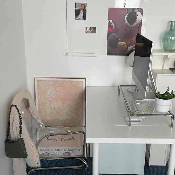White-toned home office space featuring a transparent chair, organized desk with computer, and art prints creating a modern atmosphere