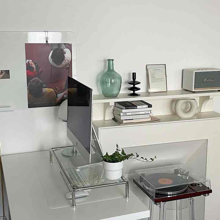 Clean modern home office space in white and green tones featuring desk with computer, turntable, and fireplace decor