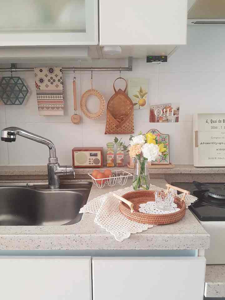 White and natural color toned kitchen featuring rattan tray, flower vase, and cozy kitchen accessories creating a warm atmosphere