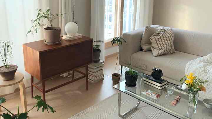 ナチュラルカラーのリビング、ベージュのソファとガラステーブル、植物と木製のコンソールが配置された雰囲気のあるインテリア