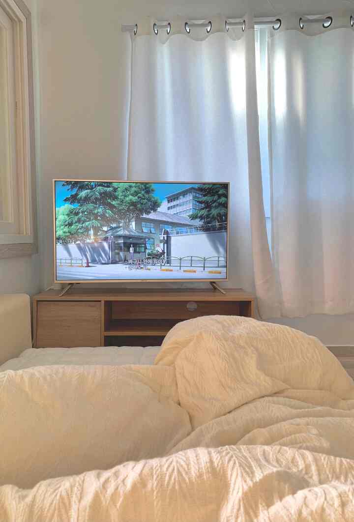 White and wood tone bedroom featuring cozy bedding and TV stand with a calm, modern atmosphere