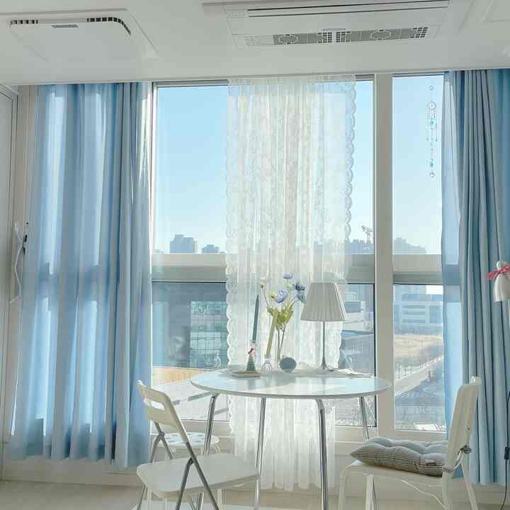 Soft sky blue and white toned studio dining space featuring round table and lace curtain with bright cozy atmosphere