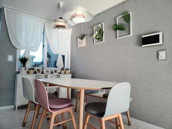 Gray-toned wall and white furniture in a 4-person dining room featuring wooden dining table and chairs, pendant lights, plant picture frames, and a natural atmosphere