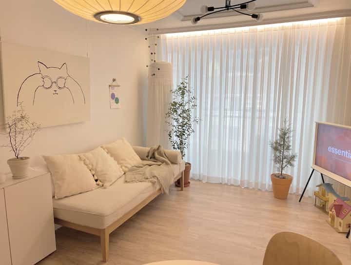 白とベージュのトーンのリビング、ナチュラルモダンなソファとカーテンが配置された雰囲気のある空間