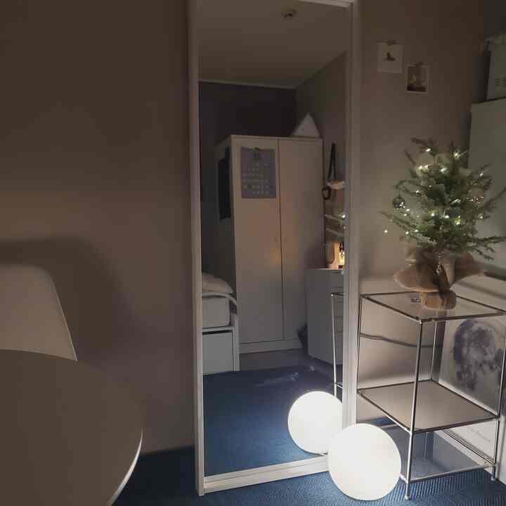 A calm dining room with navy rug and white furniture, featuring a full-length mirror and lighting creating serene modernity
