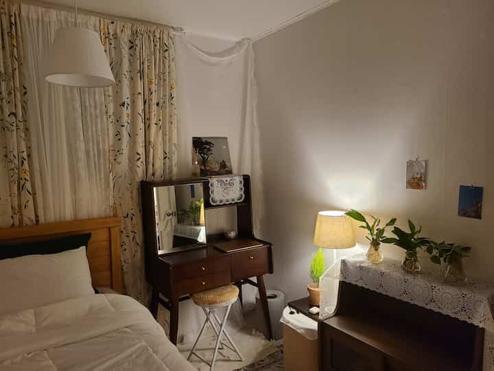 白とベージュの色調の寝室、木製の化粧台とベッド、パターンカーテンが配置された雰囲気のある北欧風インテリア