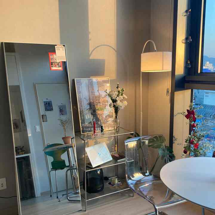 ホワイトとシルバーのトーンのワンルーム、モジュラーシェルフとフロアランプが配置された自然でコンパクトな雰囲気のインテリア