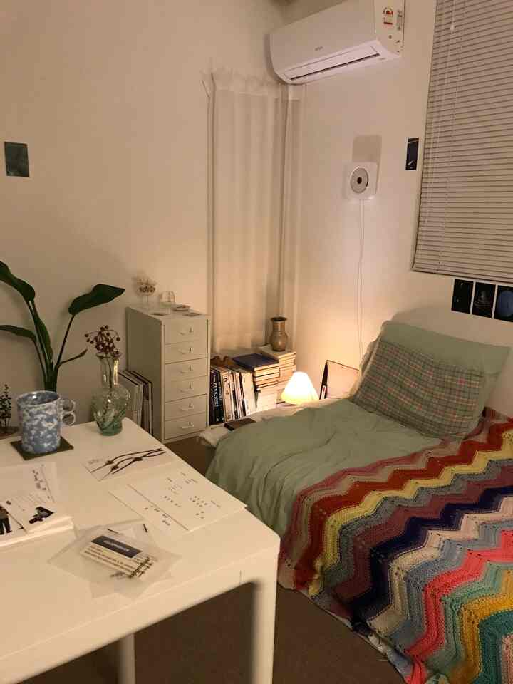 Cozy white and green toned single household bedroom with a desk and storage cabinet in a natural modern style
