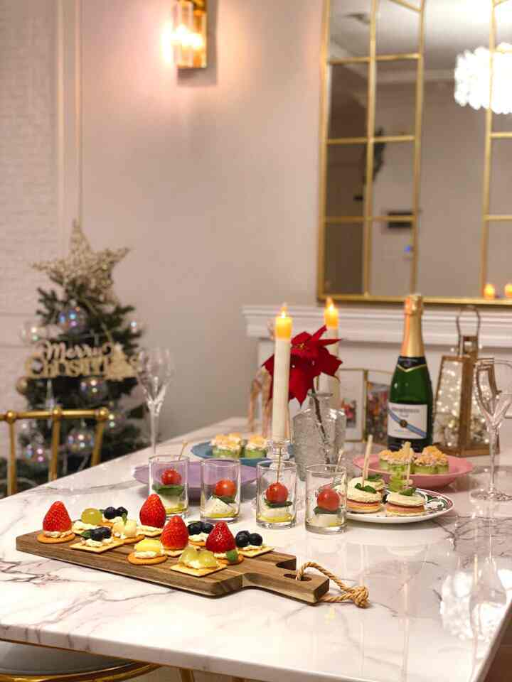 白とゴールドのトーンが特徴のリビングルーム、クリスマスの装飾とフィンガーフード、キャンドルが配置された雰囲気のあるホームパーティー空間