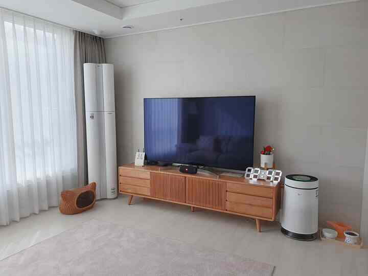 ホワイトの壁とカーテンのリビング、ウッドトーンのテレビ台とペット用品が配置された清潔感のある空間