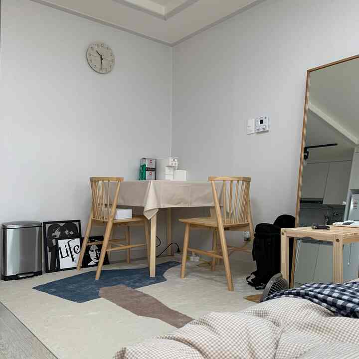 White and wood tone studio apartment dining area featuring a simple dining table, chairs, wall clock, and a full-length mirror with a clean atmosphere