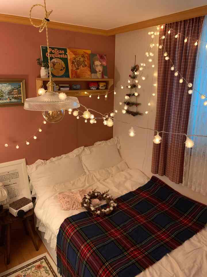 Cozy bedroom with warm wood tone walls, checked curtains, white bedding, and Christmas decorations including snowflake string lights