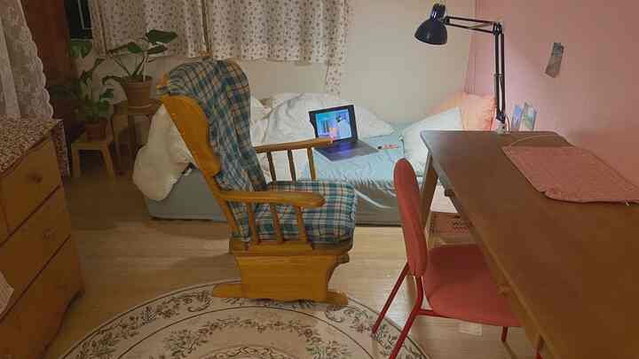 Natural-tone bedroom featuring vintage rocking chair, round floral rug, wooden desk, and potted plants in a cozy arrangement