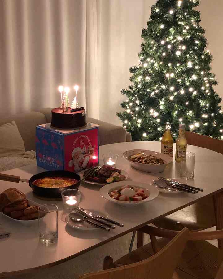 Cozy living room home party featuring a white oval table set with food, candles, drinks, and a warmly lit Christmas tree