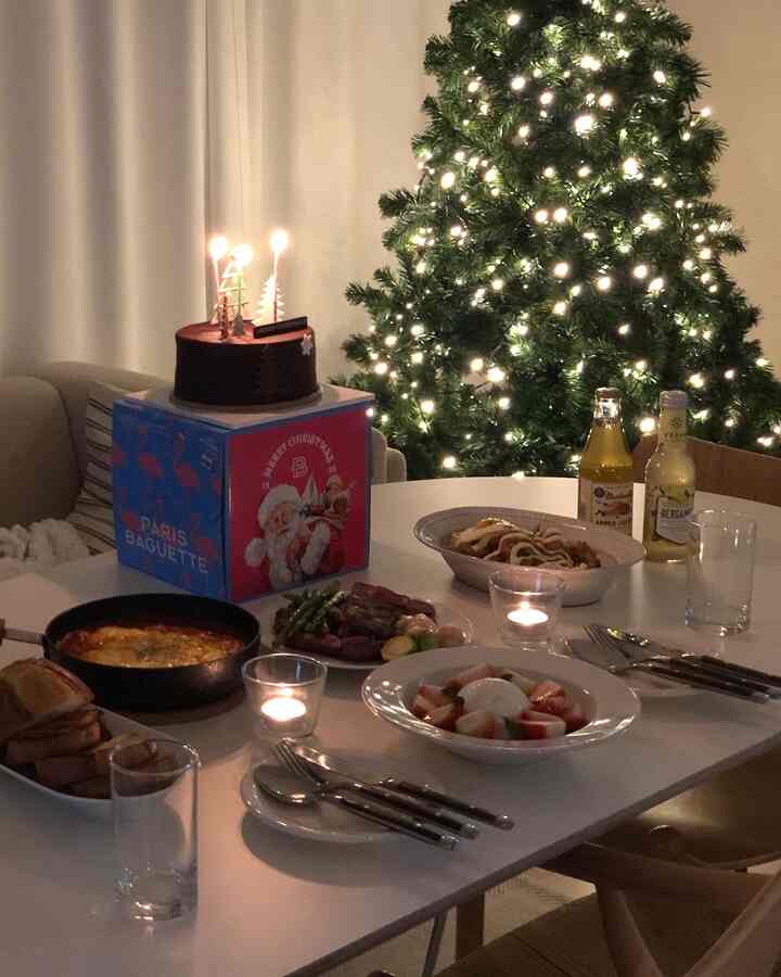 暖かい照明と白いダイニングテーブル、クリスマスツリーが配されたシンプルなダイニングルームのホームパーティー空間