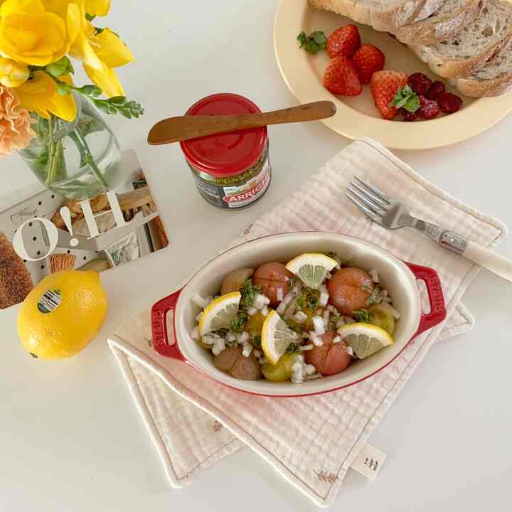 Minimal home cafe setting on a white table featuring a red ceramic gratin dish with salad, fresh fruits, and bread for a cozy meal