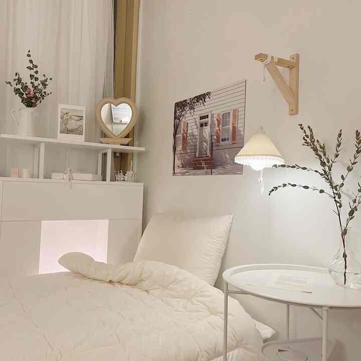 White-toned bedroom featuring white bedding, nightstand, poster, and hanging shade light creating a warm atmosphere