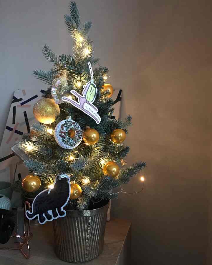 A green mini Christmas tree decorated with gold ornaments and string lights placed on a wooden table creating a cozy atmosphere