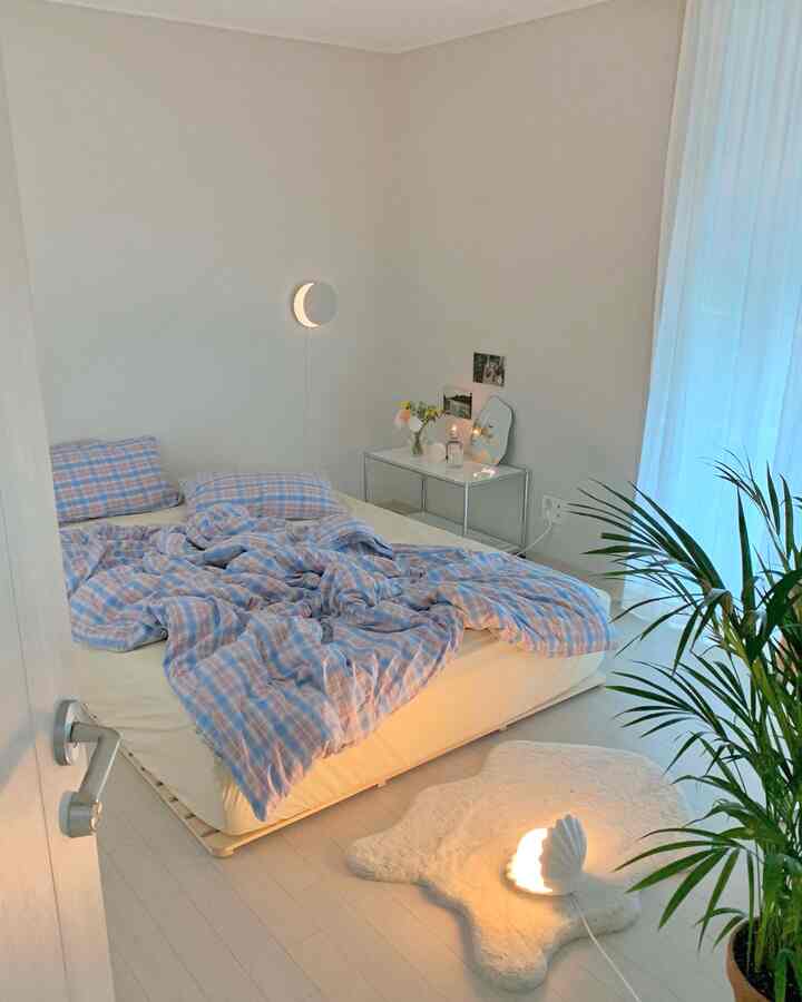 Bright natural-toned bedroom featuring a bed with checkered bedding, mood lighting, a rug, and plants creating a warm atmosphere
