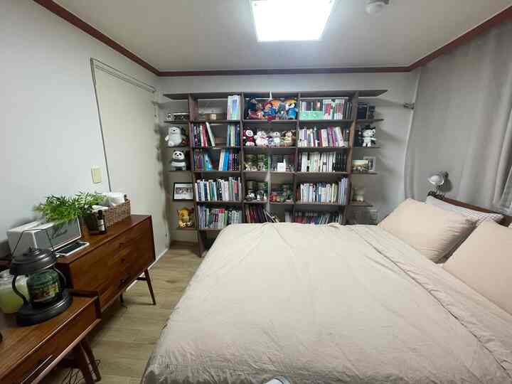 Natural beige and wood-tone bedroom featuring a large bed, extensive bookshelf, and wooden dresser creating a cozy atmosphere