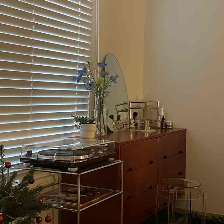 Cozy space with wood tone dresser topped by mirror and flowers, featuring natural beige walls and blinds