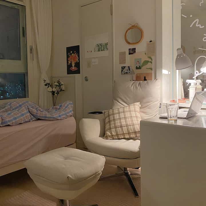 Natural-toned studio bedroom featuring a cozy armchair, desk with laptop, and bed creating a warm ambiance