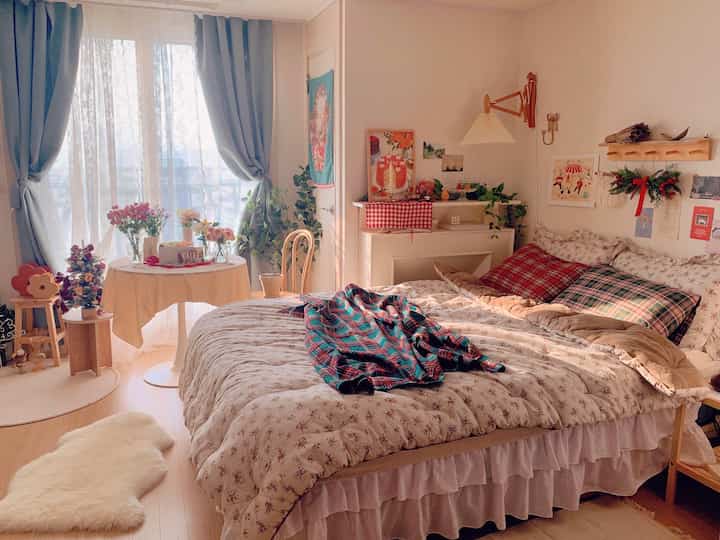 居心地の良いベージュ調の冬の寝室、花柄の寝具とブルーのカーテン、小さな丸テーブルと壁暖炉が配置された雰囲気のあるインテリア