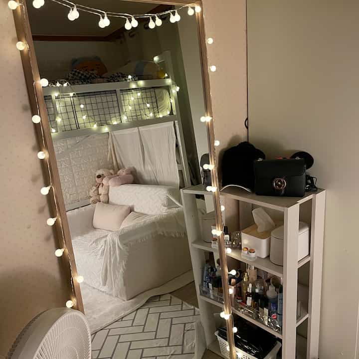 白とナチュラルカラーの寝室、二段ベッドと全身鏡、ストリングライトが配置された雰囲気のあるインテリア