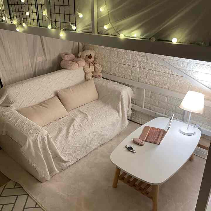 アイボリーと自然な色調の4.5畳のコンパクトな部屋、ソファベッドと白いテーブル、照明とクッションが配置された雰囲気のあるインテリア