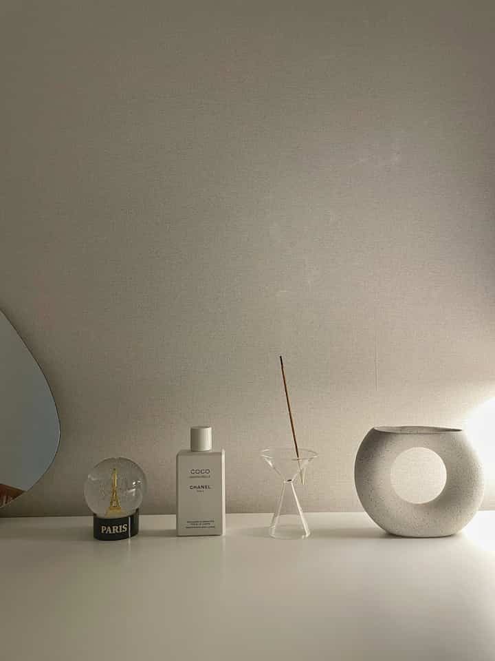 ベージュとホワイトのトーンの寝室のテーブルに、ミニマルな花瓶やインセンスホルダーが配置された雰囲気のあるインテリア