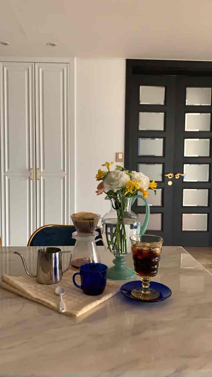 Cozy home cafe kitchen featuring a marble dining table with a drip coffee set and a vase of flowers