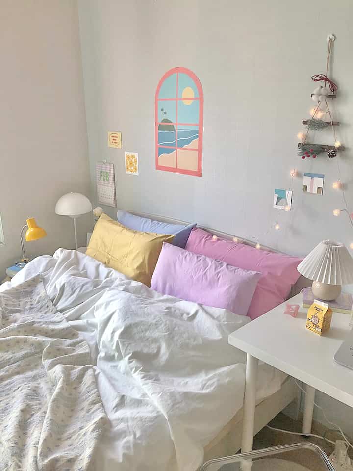 A cozy bedroom space with soft white and pastel-toned wallpaper, featuring eye-catching yellow and pink pillows in a cotton candy vibe