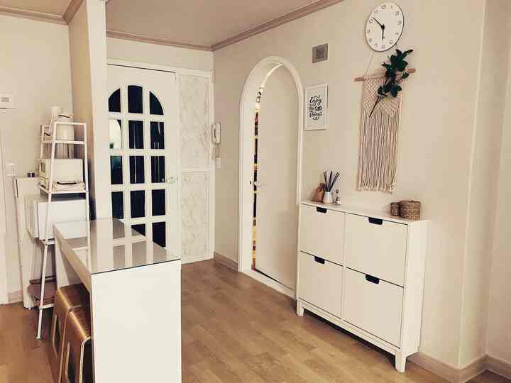 White and beige entrance space featuring a shoe cabinet and macrame wall hanging with a simple, modern atmosphere