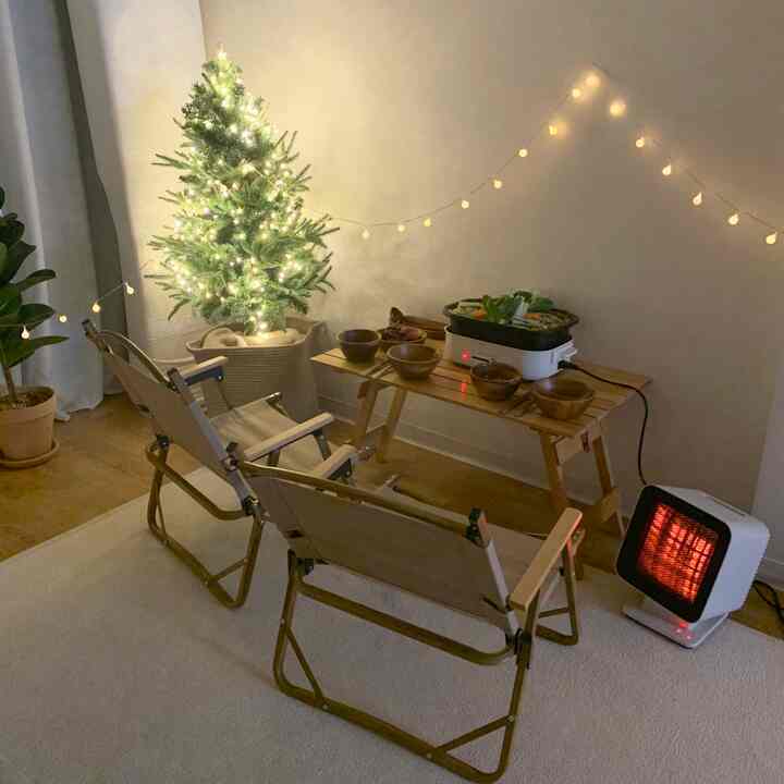 Warm wood tone and white living room space featuring a Christmas tree and camping chairs creating a home party vibe with an electric heater providing warmth
