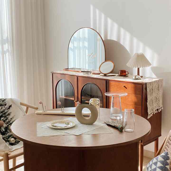 Bright dining room with white walls, curtains and natural brown wood round table and sideboard with decorative elements