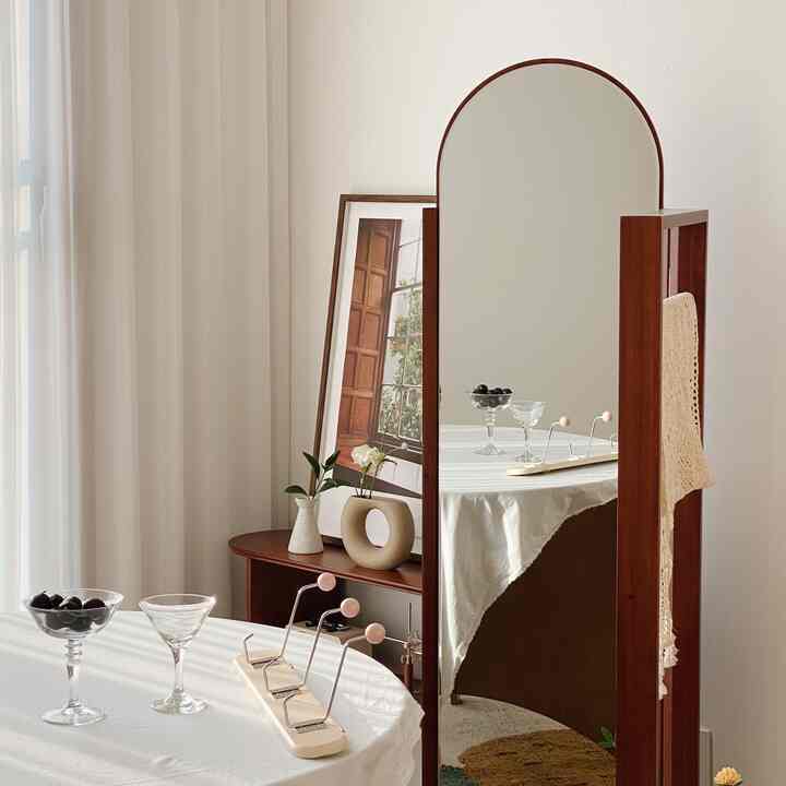 A white-toned living space featuring a wooden full-length mirror and round table, creating a warm and serene interior