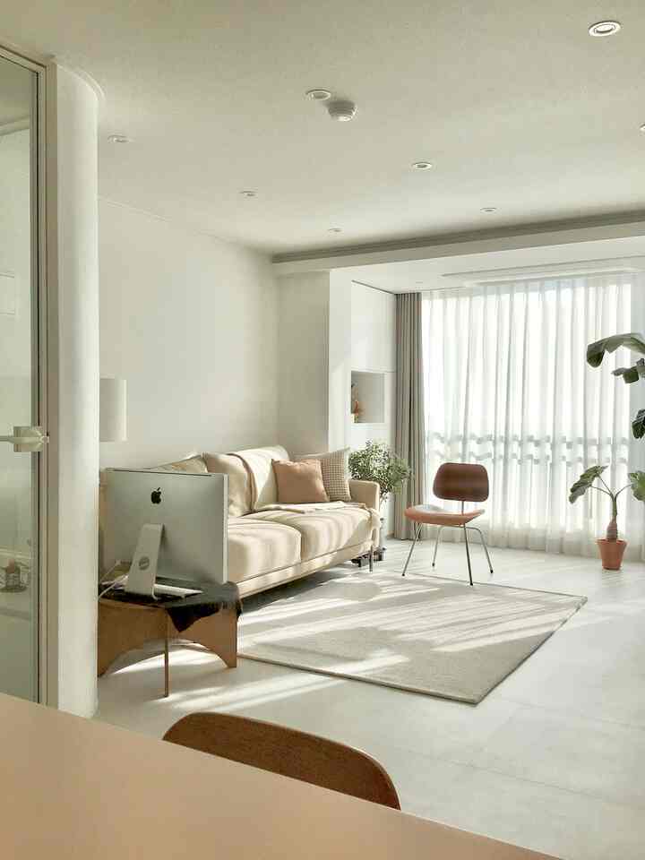 Bright white and beige living room featuring beige sofa, sheer curtains, and plants creating a natural modern atmosphere