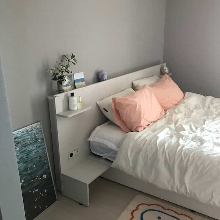White and natural color-toned bedroom featuring pink pillows and a poster, creating a cozy atmosphere