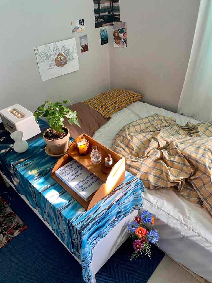 ナチュラルなトーンとブルーのアクセントが調和するワンルームの寝室、ベッドと装飾されたテーブルが居心地の良い雰囲気を作り出している。