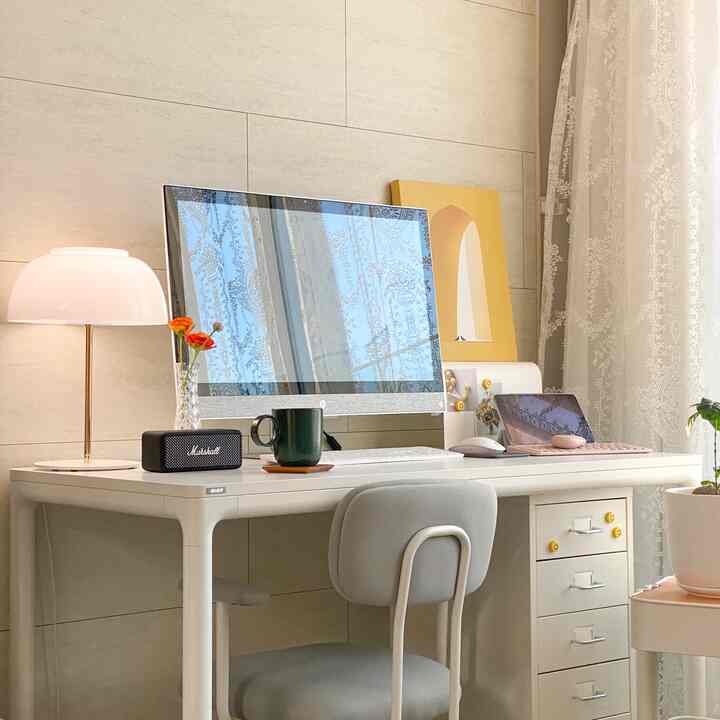 Bright natural-toned living room home office featuring a white desk with drawers and lace curtains creating a cozy workspace