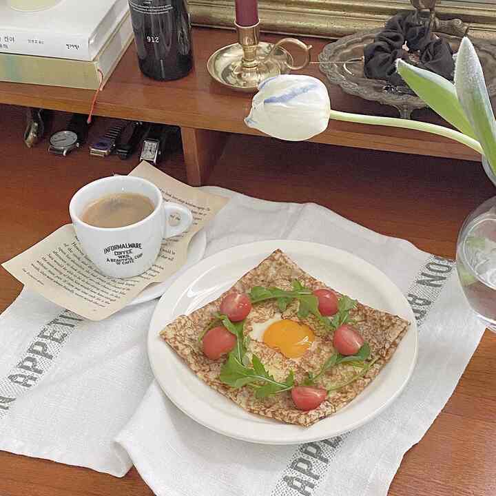 白と茶色の色調のデスクにコーヒーとクレープ、花瓶が配置された雰囲気のあるカフェ風インテリア