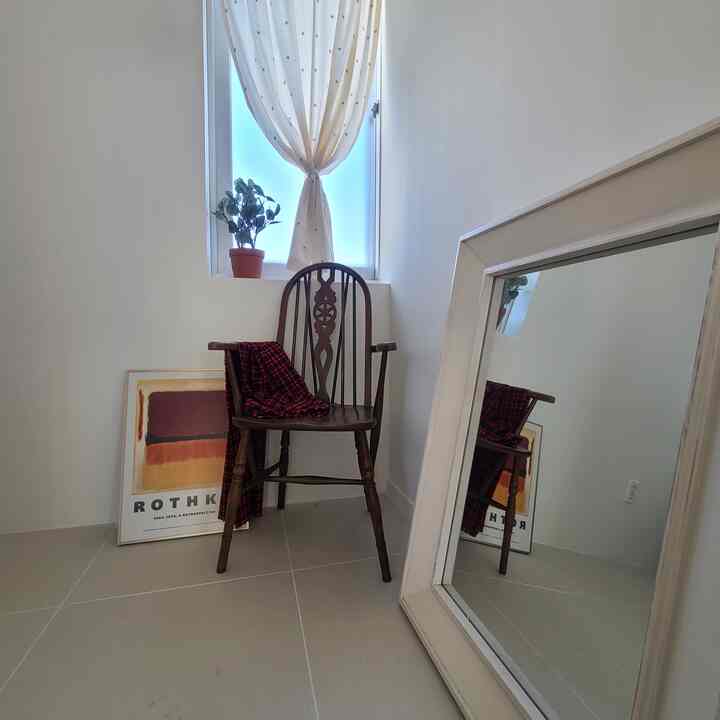 White tone dining room entrance featuring a wood-tone armchair, curtain, and framed art in a clean space