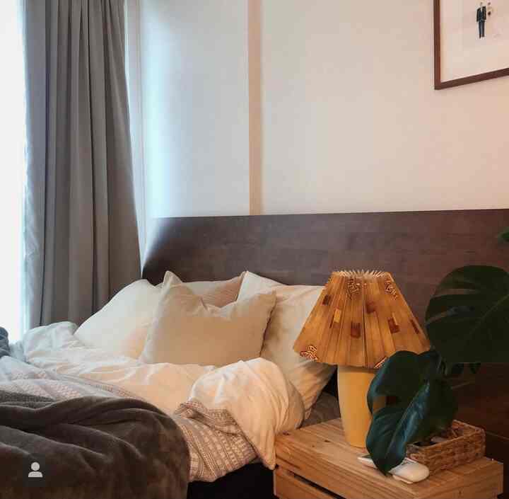 ナチュラルなブラウンウッドトーンとベージュの寝室、クイーンサイズのベッドと枕、暖かい照明とカーテンが配置された心地よい空間